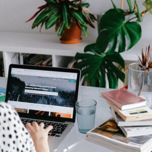 A woman working from home on her laptop surrounded by plants and books for a cozy office feel.